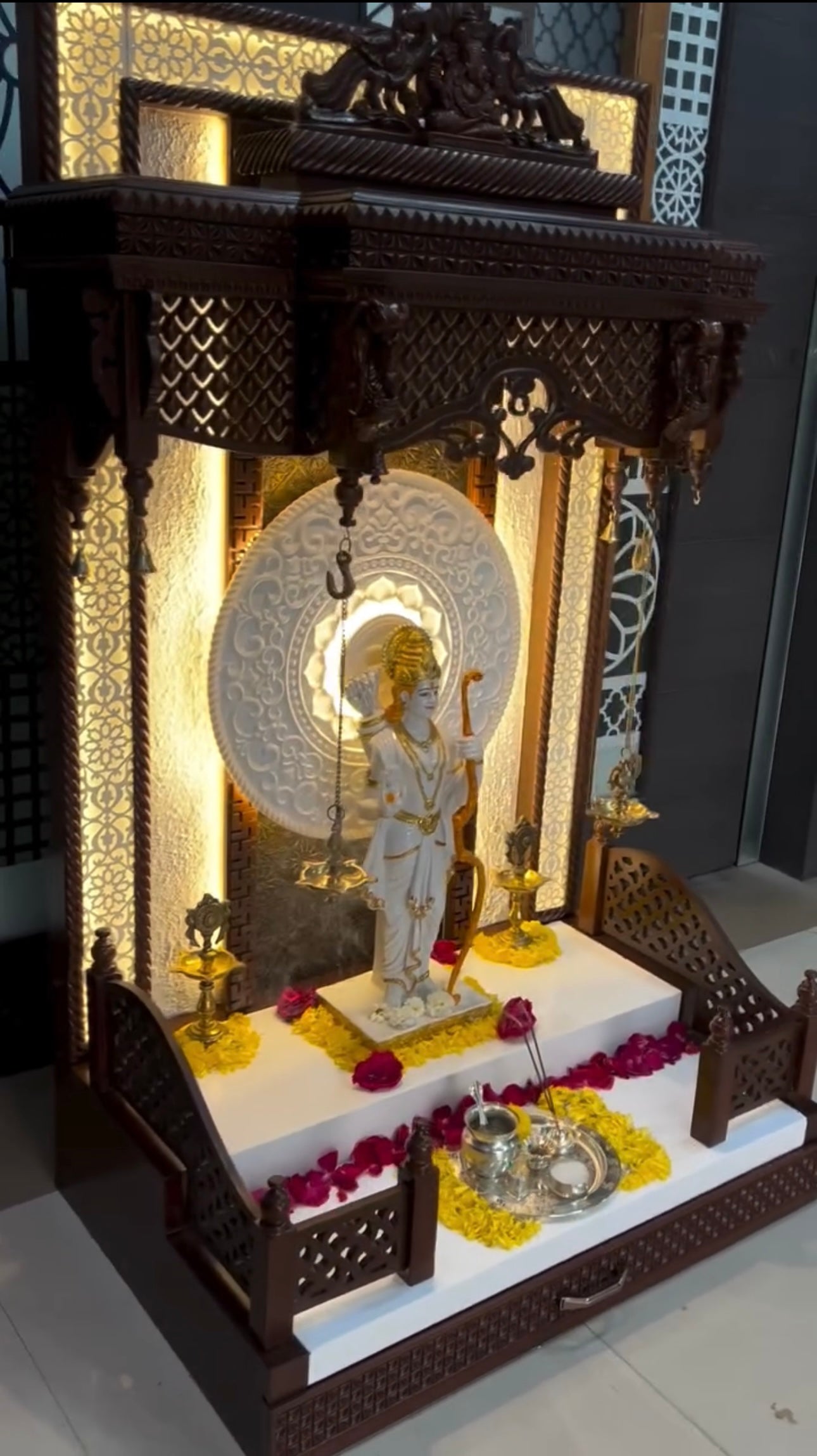Luxury wooden pooja mandir with white marble platform, decorative floral backdrop, and divine Lord Ram statue for spiritual home decor.