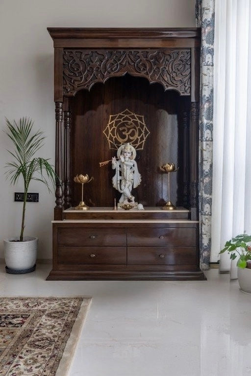 Spiritual wooden temple with Krishna idol, ornate top carving, and surrounding indoor plants for a serene home altar setup.