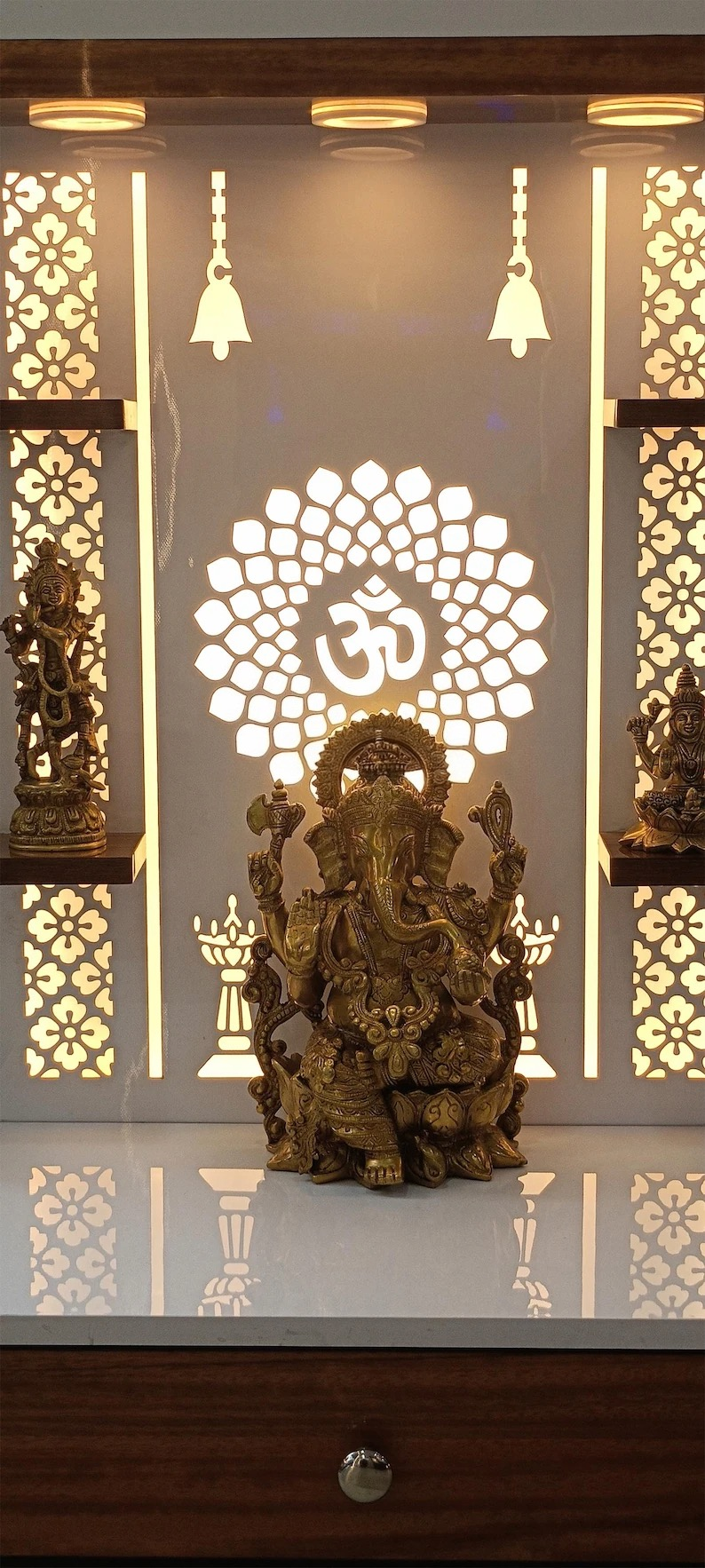 Brass Lord Ganesha idol placed on contemporary wooden mandir platform with glowing back panel and elegant traditional carvings.