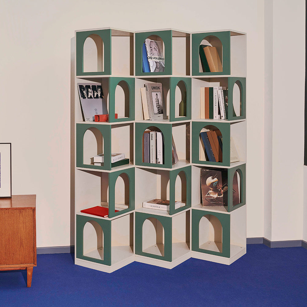 Contemporary modular bookcase with green arches, filled with books and decor, placed in a stylish interior with a blue floor and cream walls.