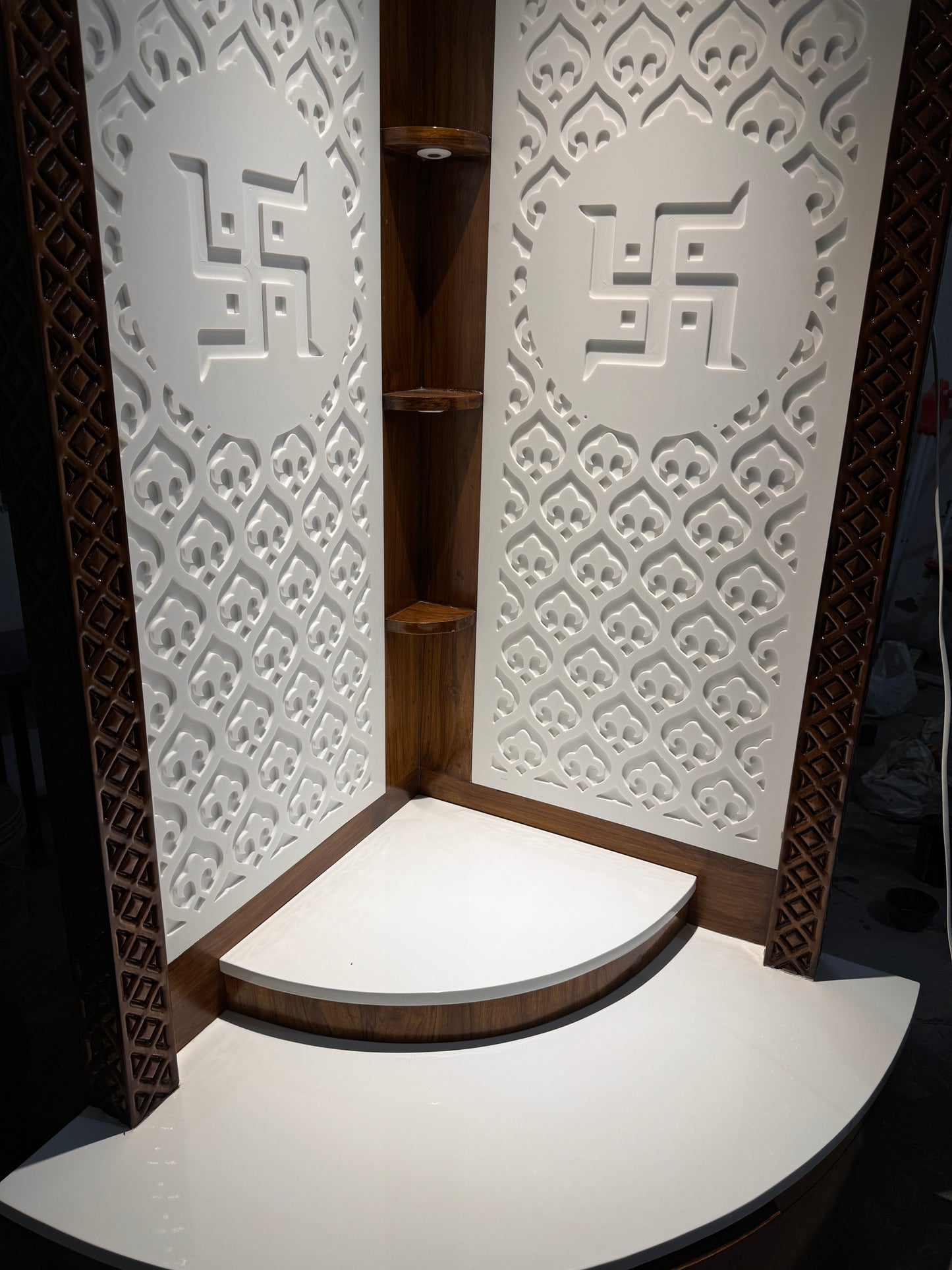 Elegant corner pooja mandir in Corian and teakwood featuring laser-engraved Swastik design and layered platform for deity placement