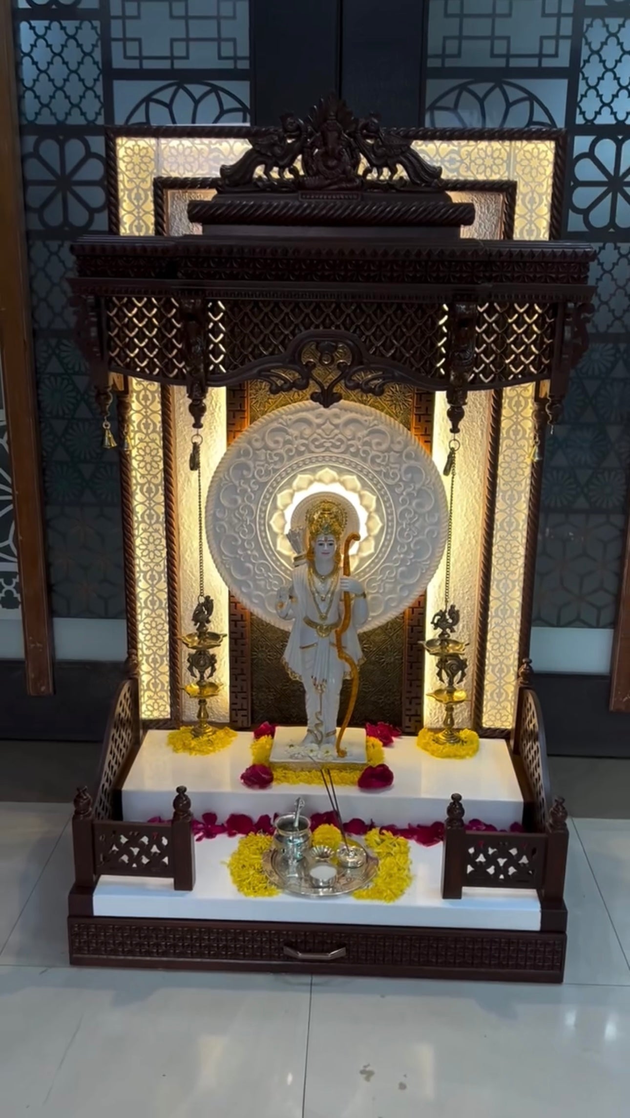 Traditional home temple made of premium wood with detailed lattice work and golden diya lamps.