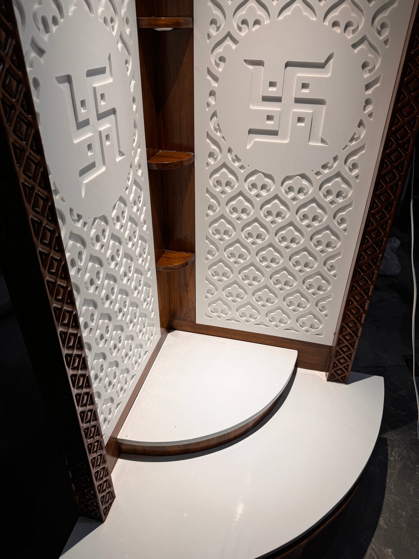 Modern luxury home temple crafted in teakwood and white Corian with 3D Swastik carvings and tiered prayer platform