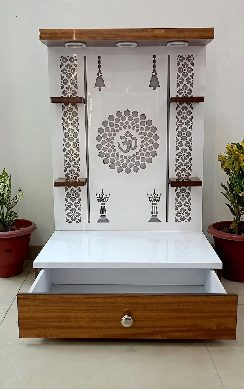 Modern wooden Pooja mandir with glossy white base and front pull-out drawer for storing pooja essentials like incense, diya, and books.