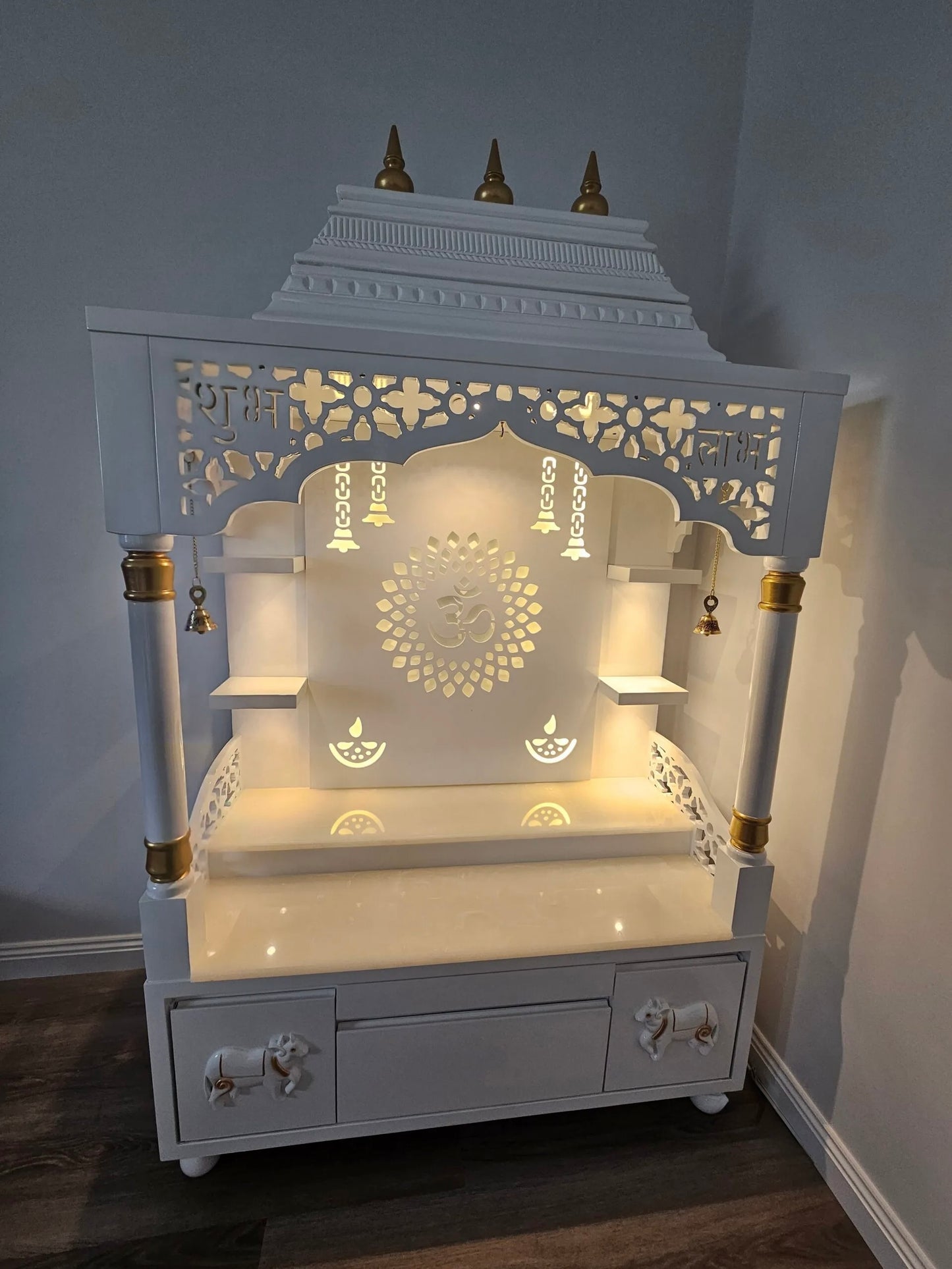White wooden pooja mandir with idols and decorative lighting, traditional home temple setup with storage drawers