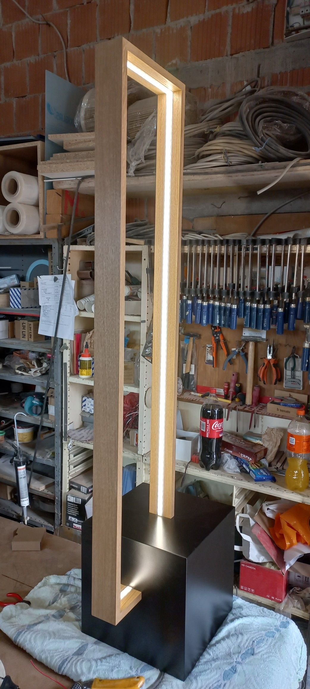 Modern floor lamp with a black base and illuminated design in a workshop setting.