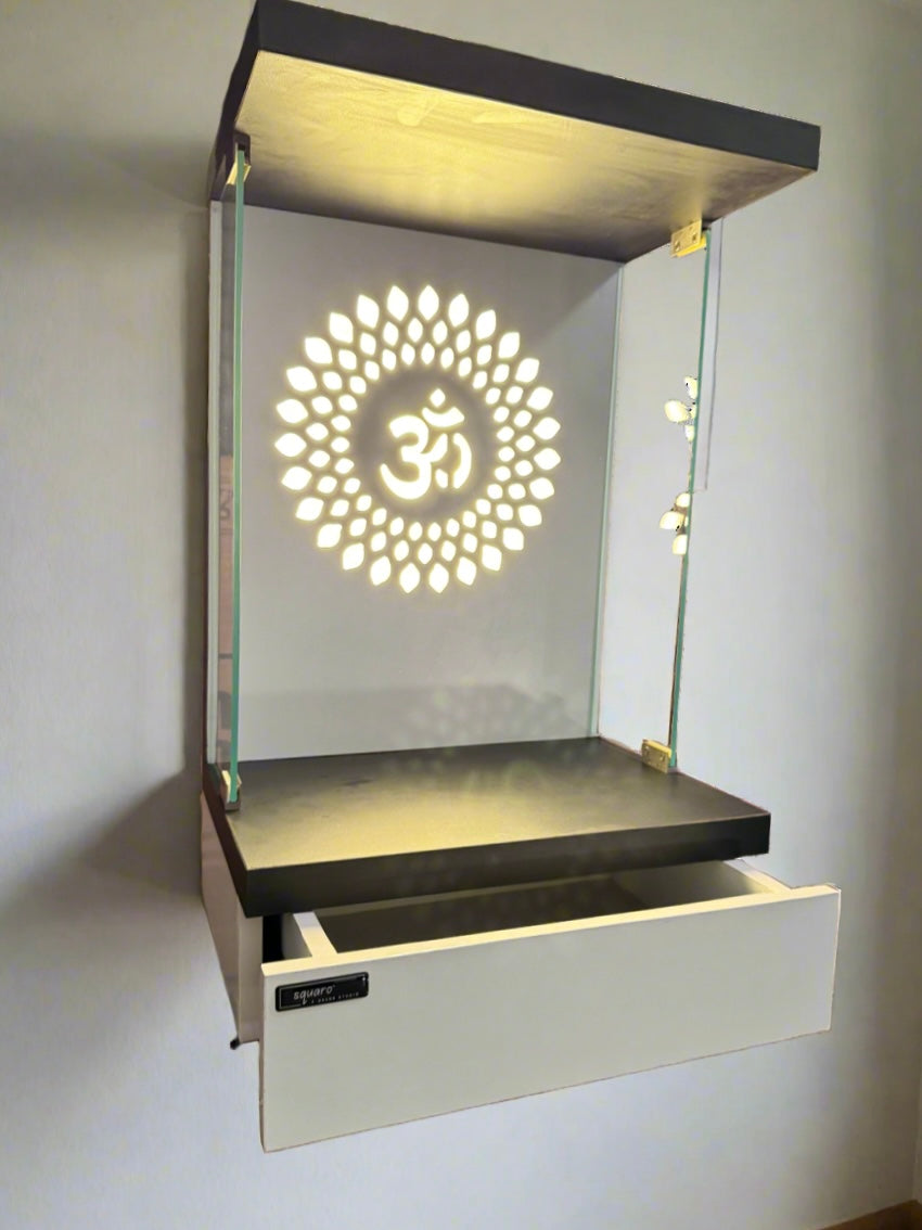 A sleek and stylish home temple featuring a warm LED-lit Om motif, glass side panels, and a pull-out storage drawer, perfect for compact and contemporary spaces.