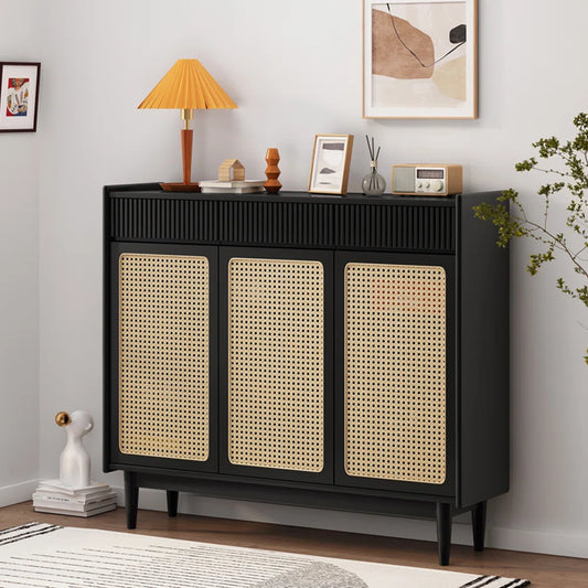 Closed black shoe cabinet with three woven cane doors, styled in a modern living room with decorative items on top.