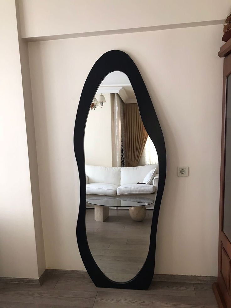 Organic-shaped standing mirror reflecting minimalist furniture and elegant interior decor.
