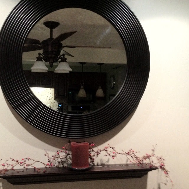 Large black circular mirror reflecting kitchen ceiling lights, styled above a mantle with candle and decor