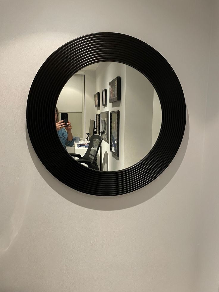 Modern round wall mirror with black ridged frame, mounted in a contemporary office space