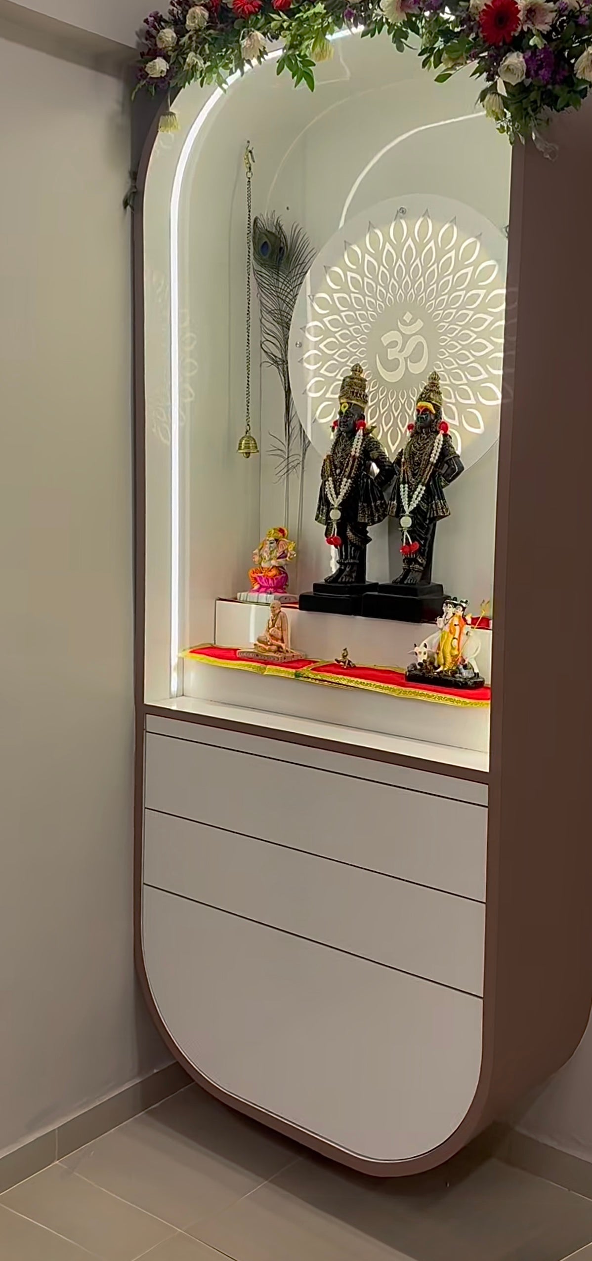 Elegant white wooden Pooja Mandir with floral arch, LED backlit Om symbol, and adorned with Vithoba-Rukmini idols and traditional Hindu deities.
