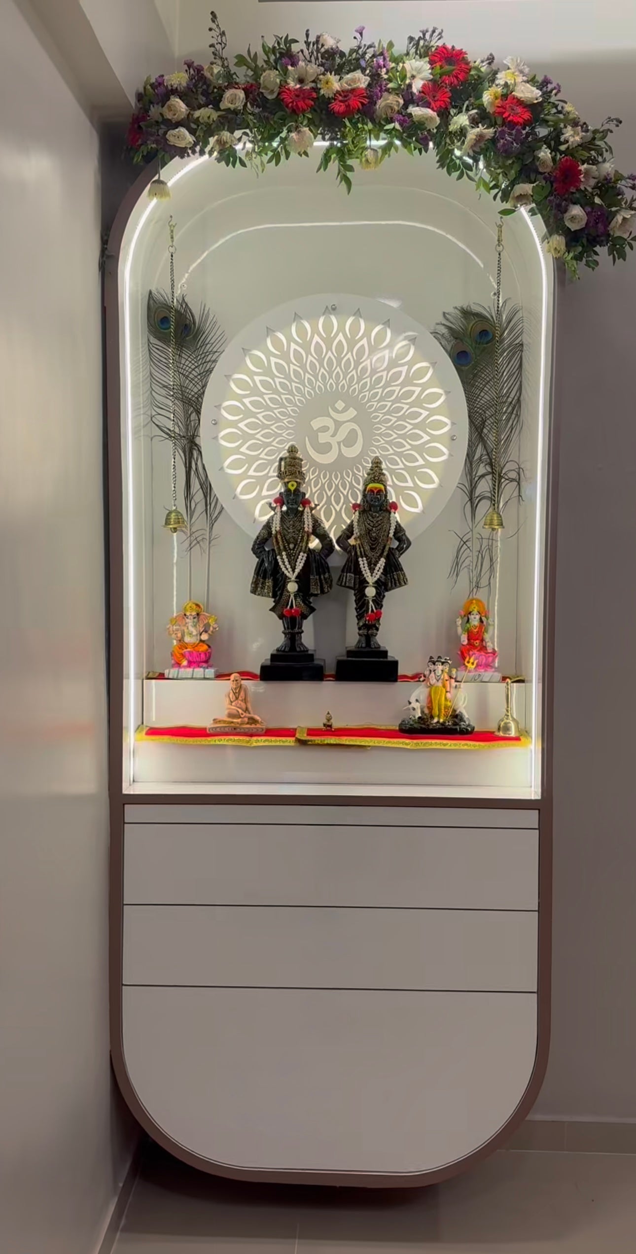 Luxurious modern Pooja Mandir featuring divine idols of Lord Vithoba and Rukmini, vibrant flower garland, and intricate lighting design for spiritual decor.