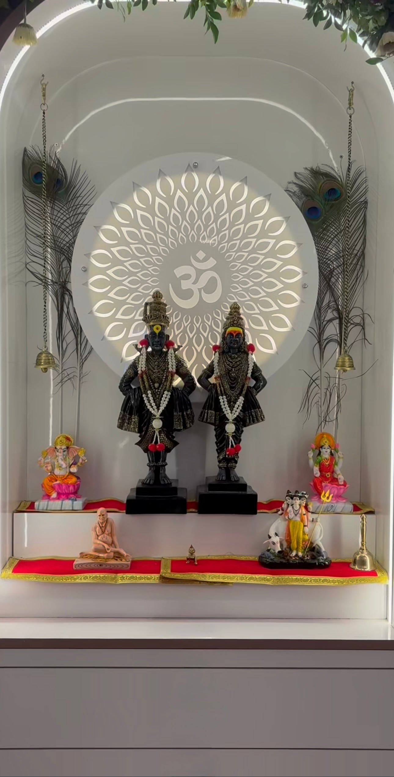 Modern wall-mounted white Pooja Mandir with floral arch, LED-lit Om design, and black Vitthal-Rukmini idols for home interior decor.