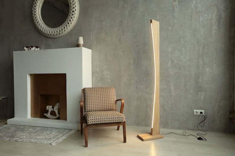 Stylish tall wooden LED floor lamp with 4000K neutral light next to an armchair in a modern interior with grey textured wall.