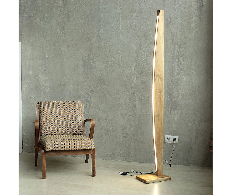 Contemporary wooden LED floor lamp next to an upholstered armchair in a minimalist living room with grey concrete wall.