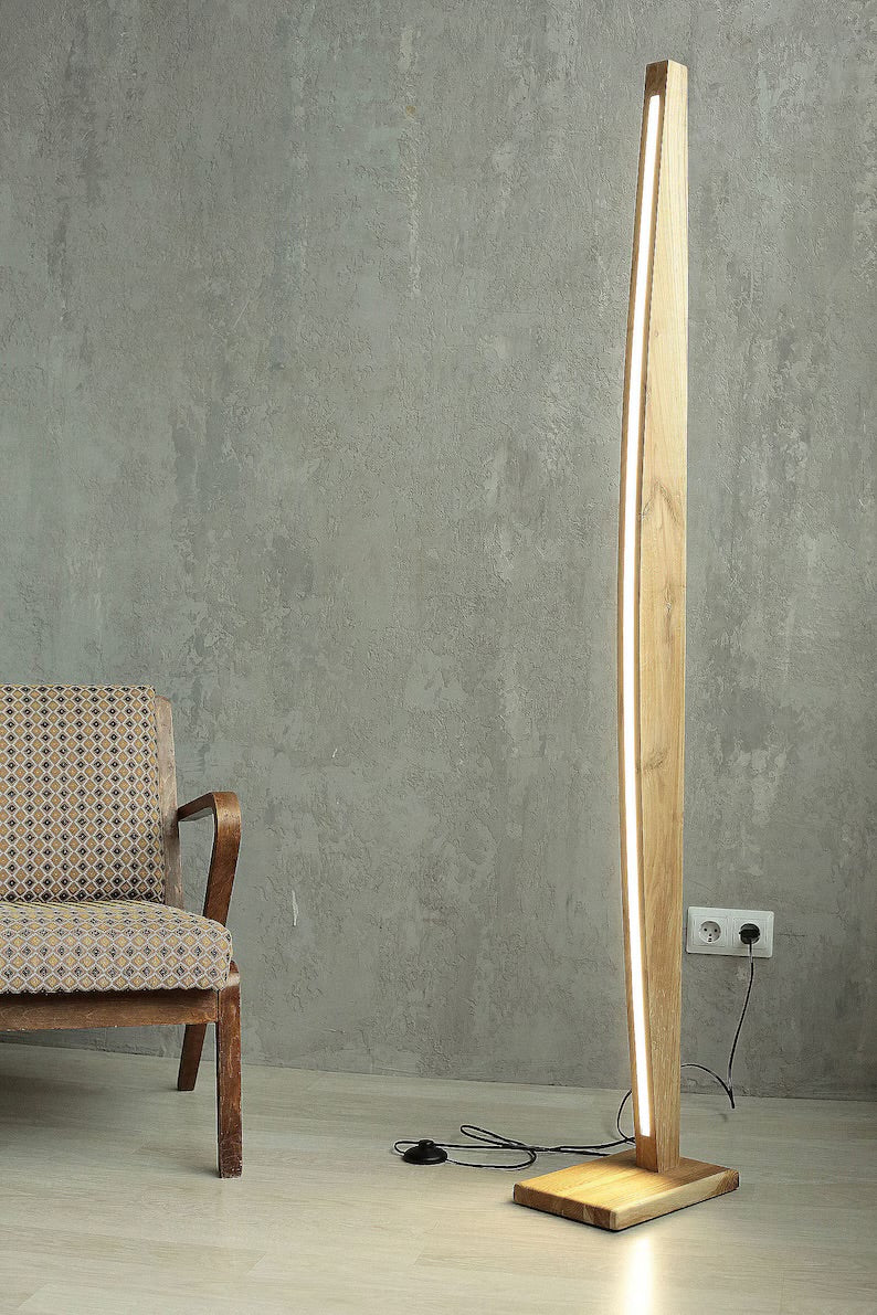 Minimalist wooden floor lamp with soft LED light, placed beside a vintage armchair against a textured concrete wall – perfect for modern interiors.