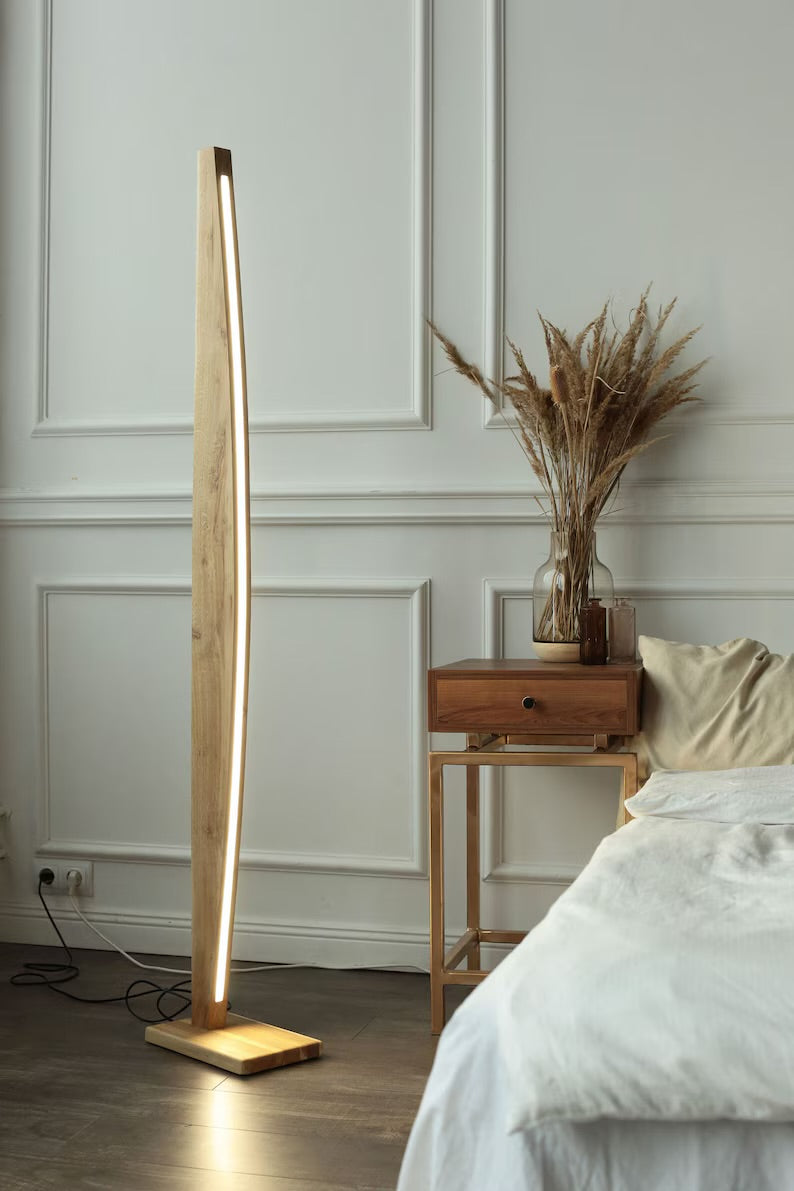 Elegant wooden standing lamp with warm LED lighting in a modern bedroom setting beside a wooden nightstand and neutral decor.