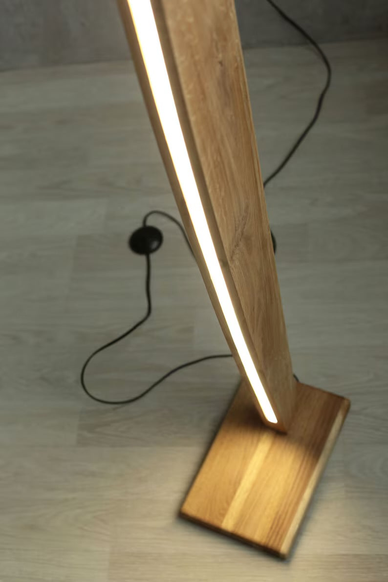 Close-up view of the wooden base and curved LED strip of a minimalist floor lamp, showcasing craftsmanship and warm ambient lighting.