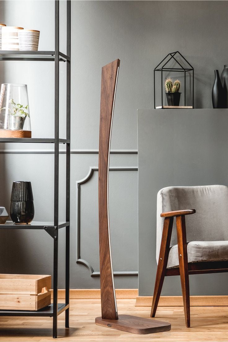 Tall modern wood LED lamp emitting warm neutral light, positioned beside a vintage armchair in a contemporary setting.