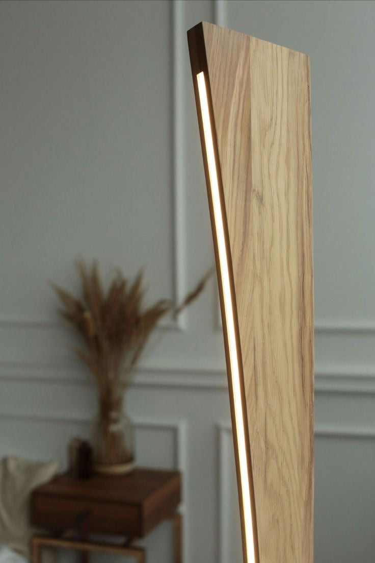 Minimalist wooden LED floor lamp with warm ambient lighting, set in a modern interior with neutral decor and natural elements in the background.