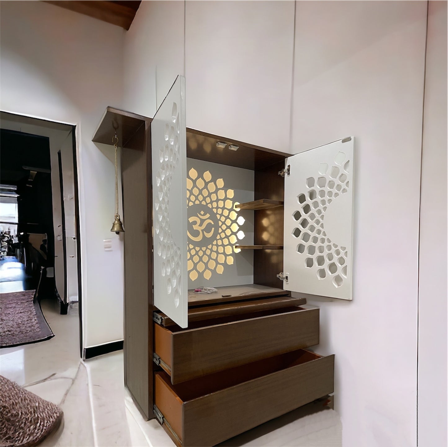 Exquisite wooden pooja cabinet with a traditional yet modern design. White doors with intricate cutwork create a beautiful lighting effect. Built-in shelves and drawers provide ample space for storing pooja essentials. The perfect blend of spirituality and aesthetics.