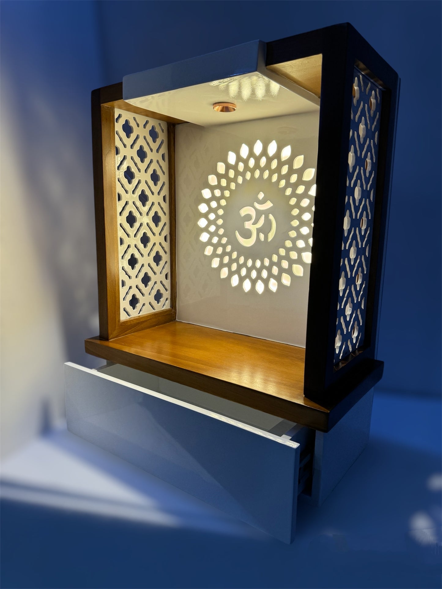 Stylish wall-mounted or tabletop home temple with a warm wooden finish, intricate jali panels, and an illuminated Om motif. Ideal for contemporary spiritual spaces.