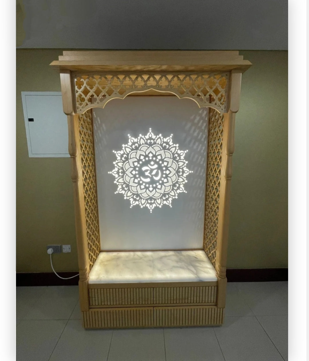 Handcrafted wooden Pooja temple with intricate carvings and illuminated Om design, creating a serene meditation space.