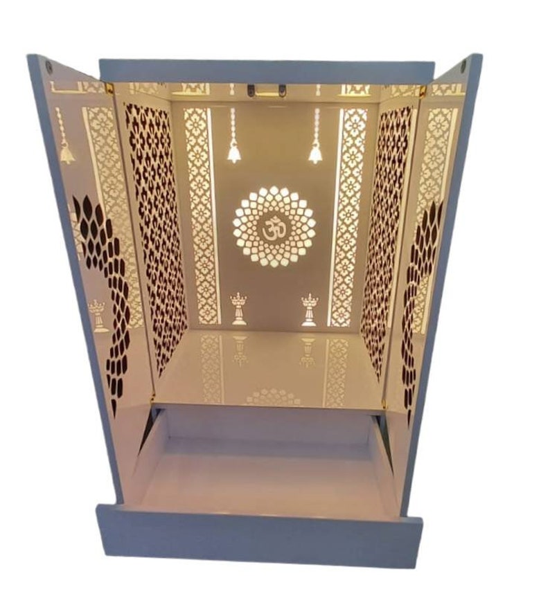 A sleek and modern pooja mandir featuring a white high-gloss finish, artistic laser-cut patterns on the doors and sides, and a spacious interior for idols and prayer essentials.