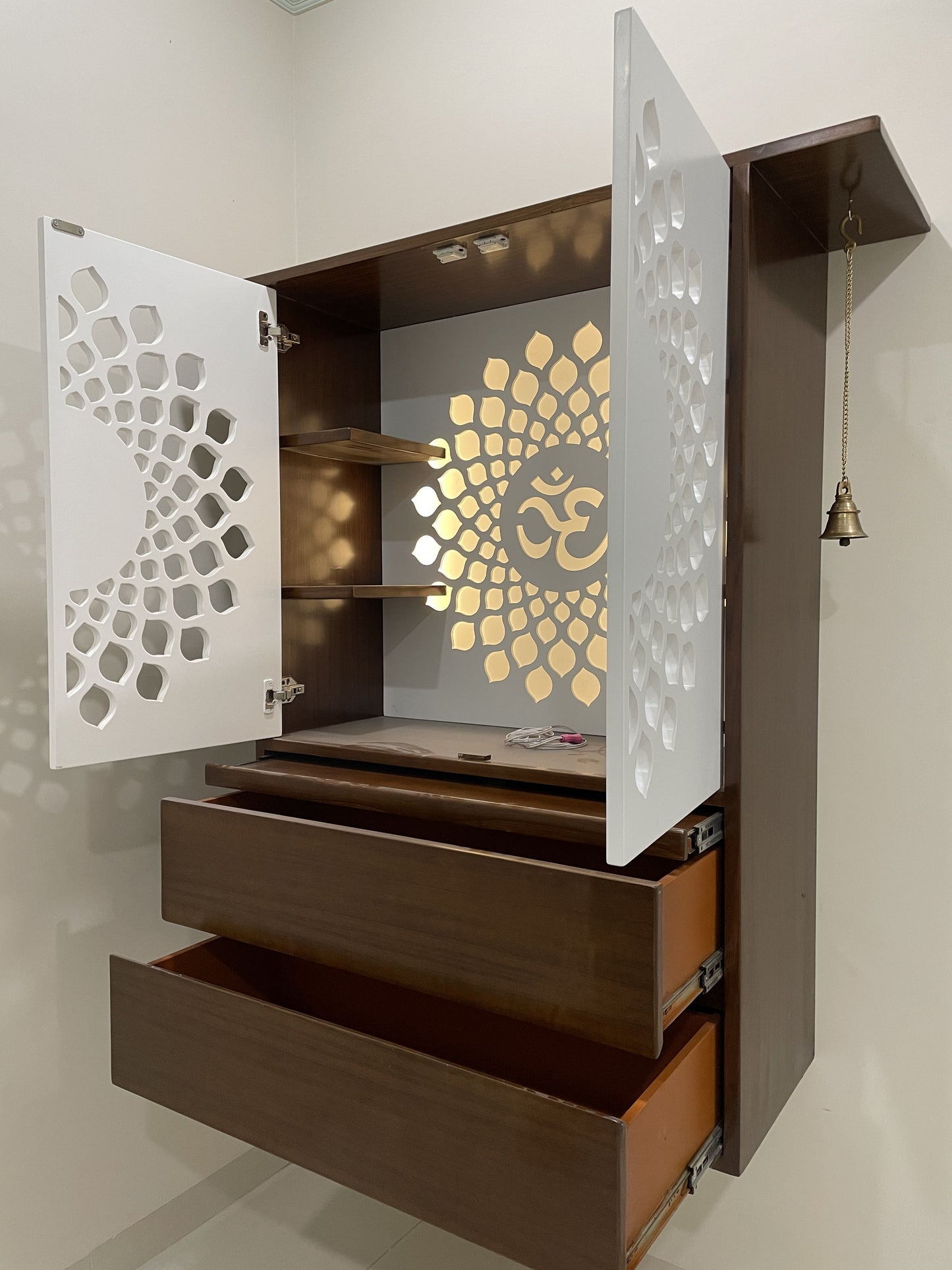 Contemporary wooden wall-mounted mandir with a beautifully illuminated "Om" design, white jali-patterned doors, and multiple storage options. Perfect for small apartments or modern prayer rooms.