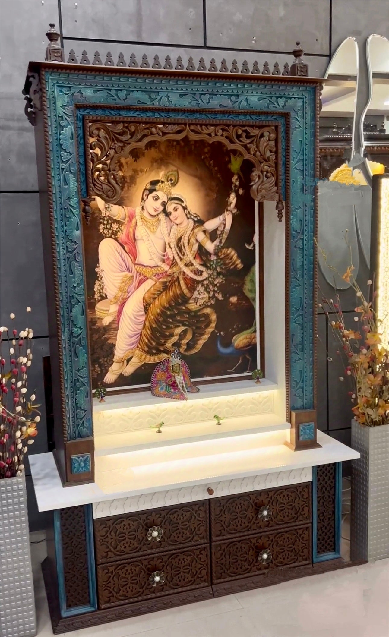 Beautiful large wooden pooja temple with a dark brown finish and peacock details, showcasing a Corian picture of Radhe Krishna alongside intricately carved drawers.