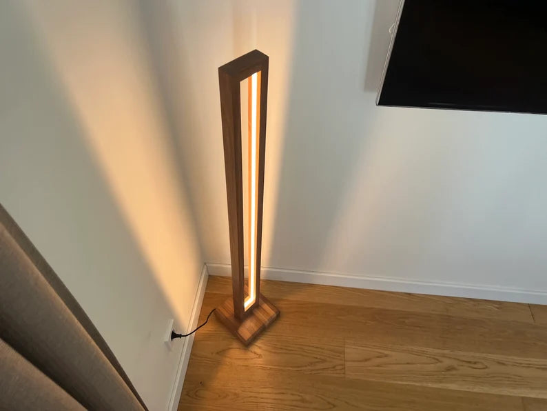 Modern floor lamp with a wooden frame and glowing light source on a wooden floor.