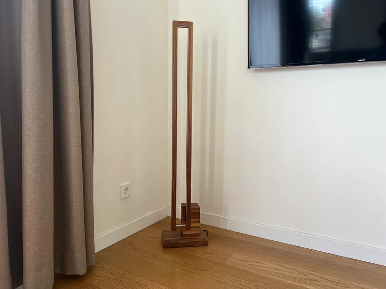 Wooden floor lamp against a white wall with a television mounted above.