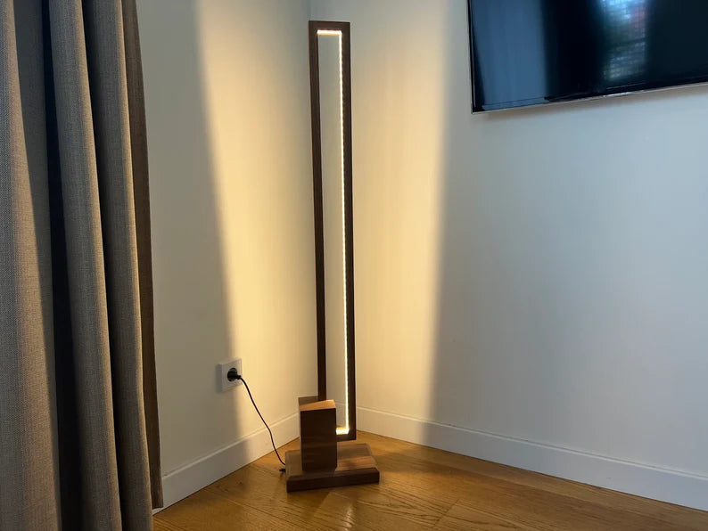 Modern floor lamp with a wooden base in a room with a television on the wall.