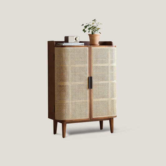 Mid-century modern closed shoe rack cabinet in solid wood with curved natural rattan doors, decorated with a plant and vintage radio on top.