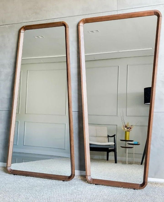 Modern full-length wooden floor mirror with trapezoid frame, leaning against wall in minimalist living space