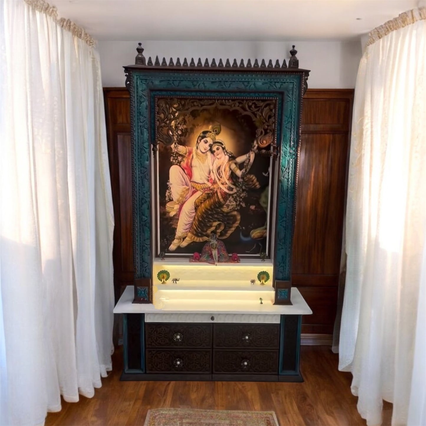 Elegant large wooden pooja temple in dark brown with vibrant peacock highlights, showcasing a Corian Radhe Krishna image and detailed drawer carvings.