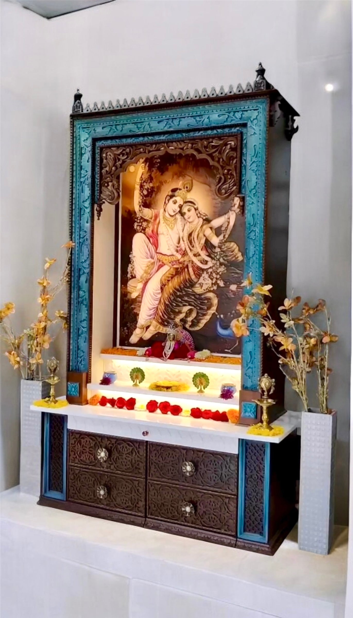 Premium large wooden pooja temple with ornate drawer carvings, dark brown and peacock hues, and a striking Corian display of Radhe Krishna.