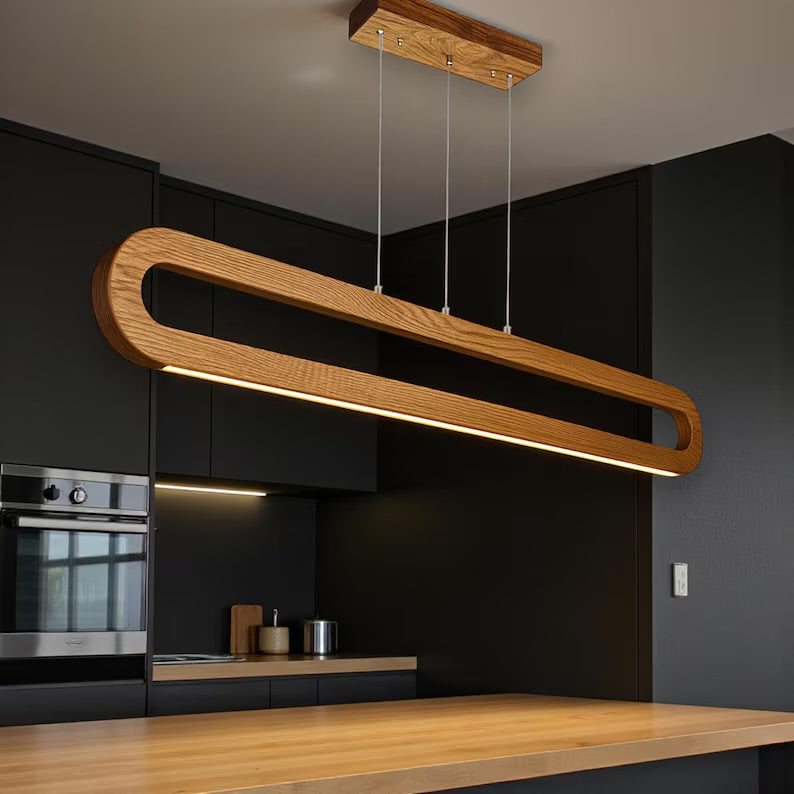 Wooden pendant light hanging above a kitchen counter with black cabinets and appliances.