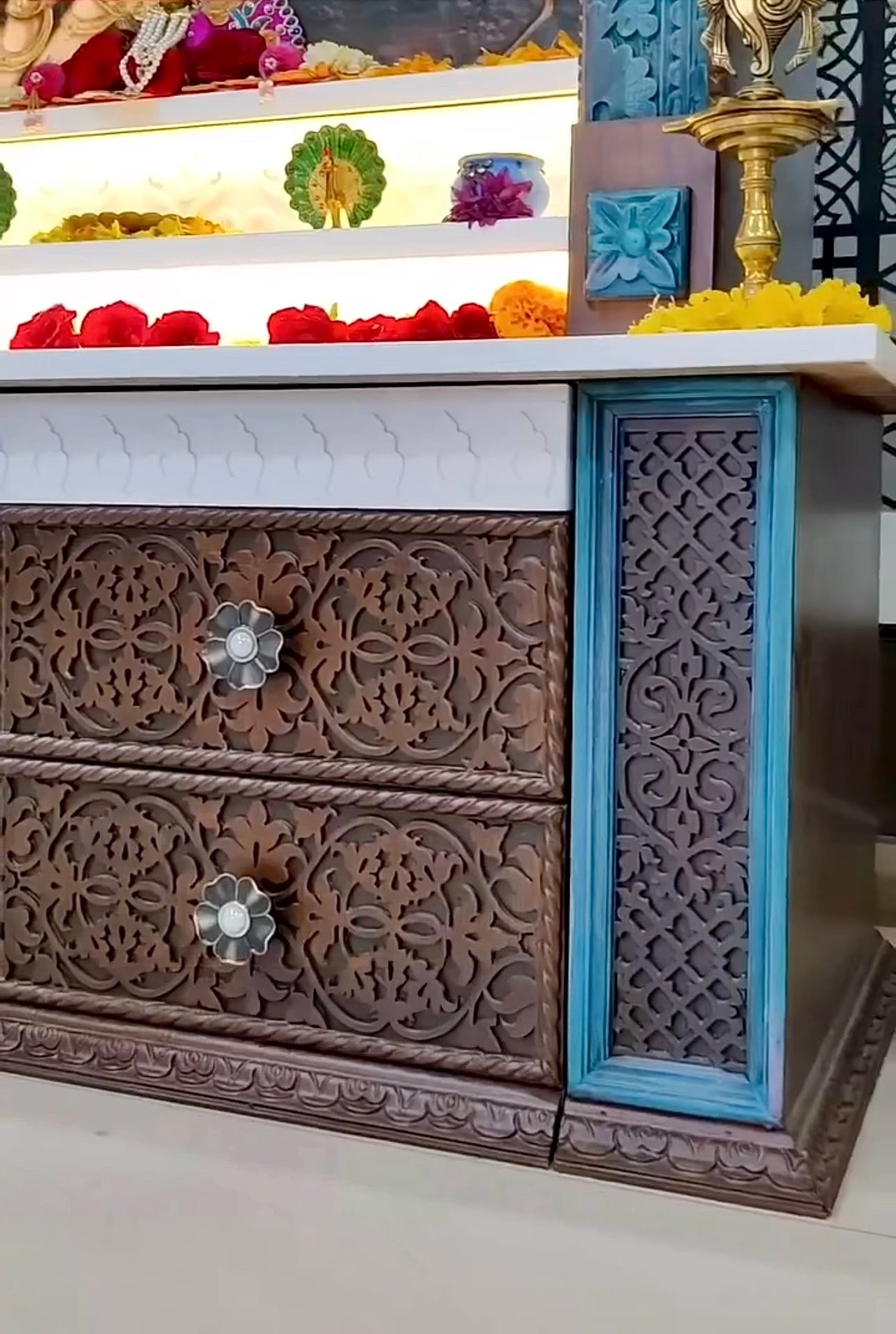 Luxurious handcrafted wooden pooja temple in dark brown with peacock accents, showcasing a Corian picture of Radhe Krishna and ornate drawer carvings.