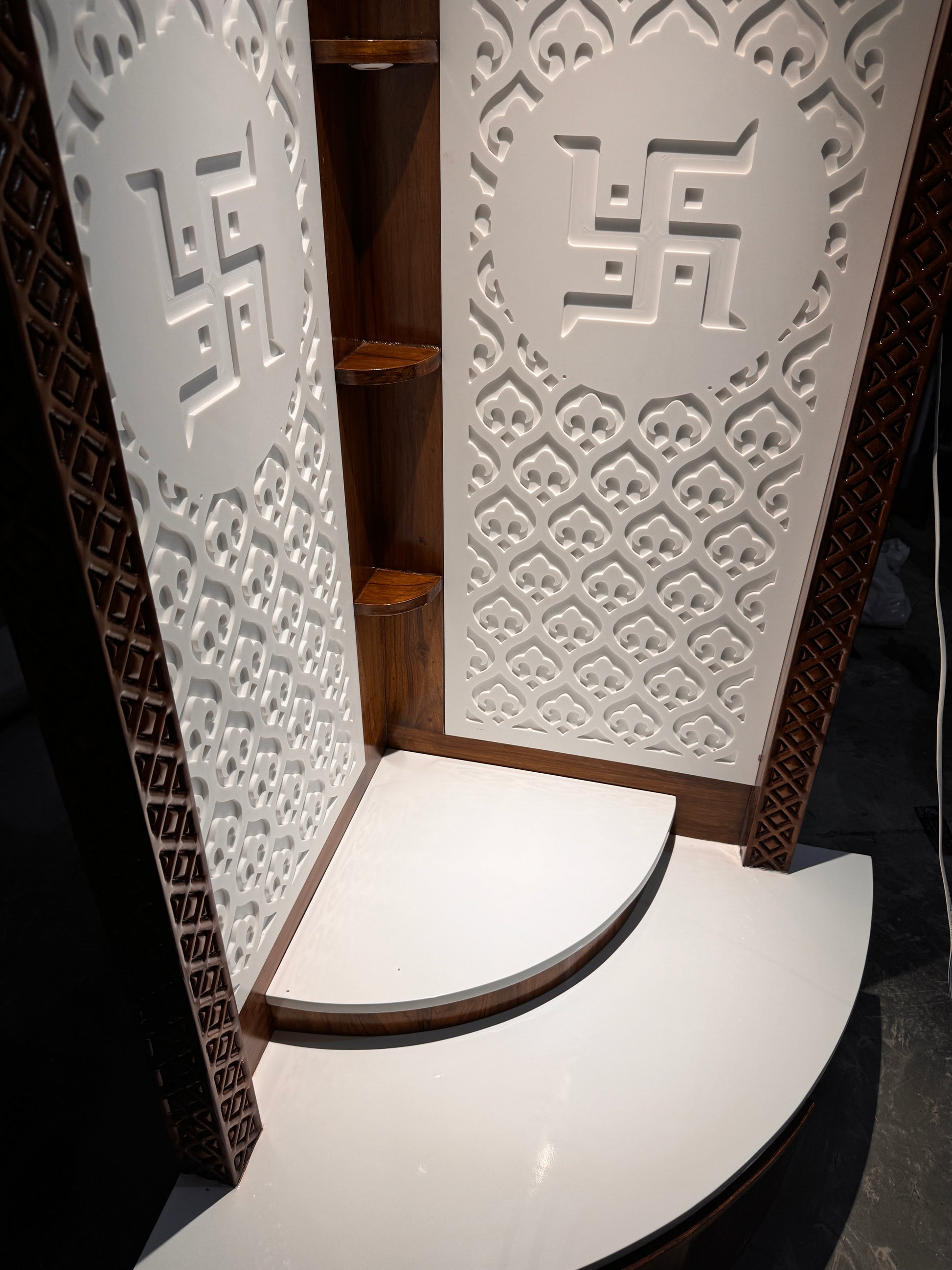 Modern luxury home temple crafted in teakwood and white Corian with 3D Swastik carvings and tiered prayer platform