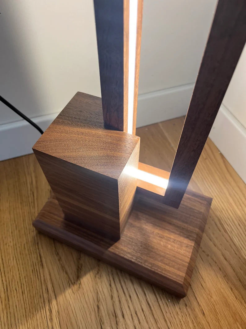 Wooden lamp with a rectangular base and vertical design on a wooden floor.