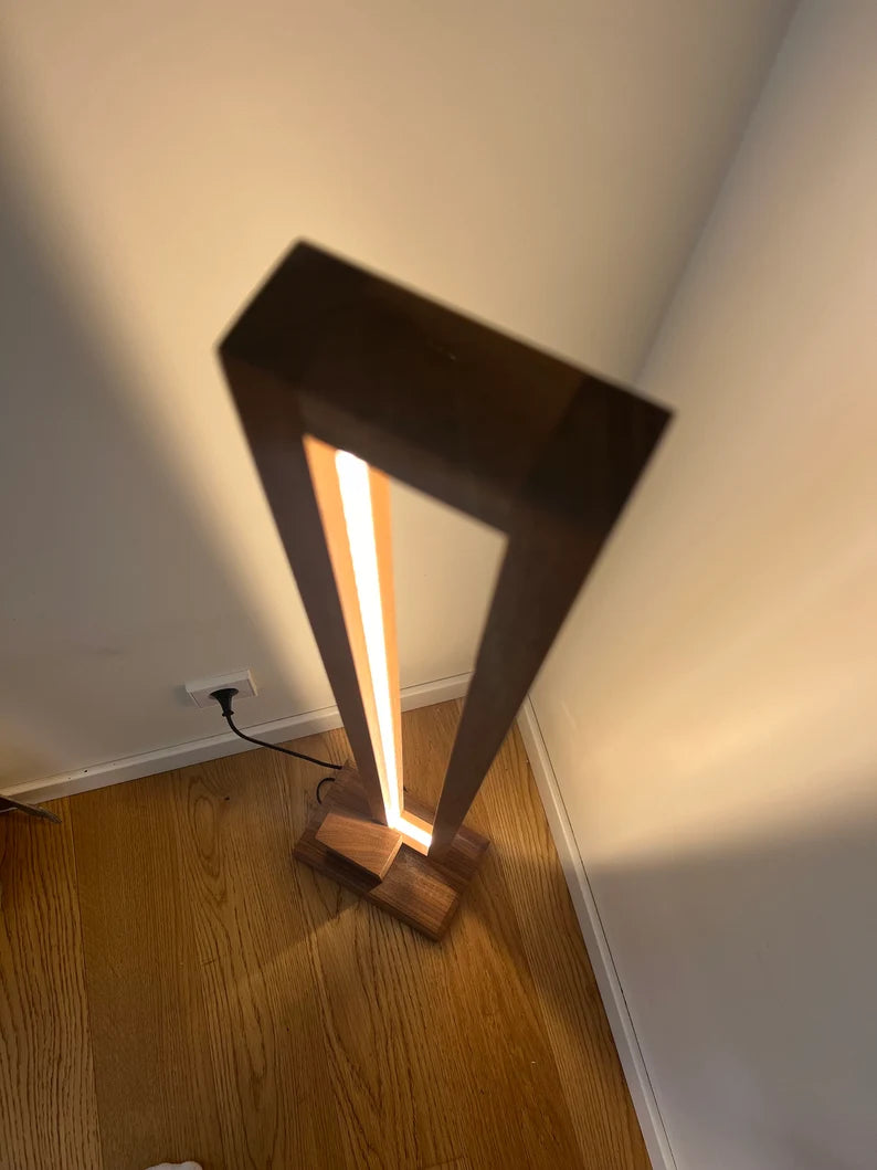 Modern floor lamp with wooden base and rectangular base on a wooden floor.