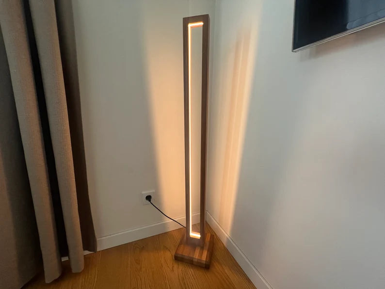 Modern floor lamp with a wooden base and LED light strip on a wooden floor.