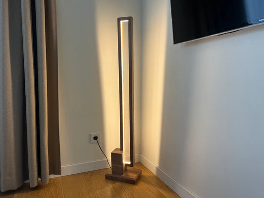 Modern floor lamp with wooden base and LED light strip on a wooden floor.