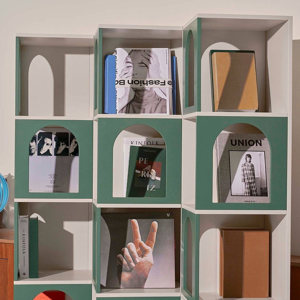 Modern bookshelf with green arch cutouts, styled with books, magazines, and decor items in a contemporary living space.