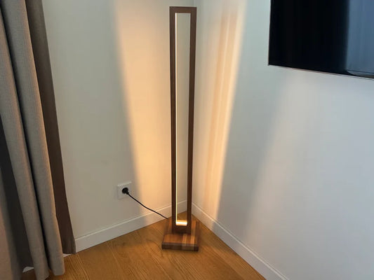 Tall floor lamp with a wooden frame on a wooden floor next to a wall.