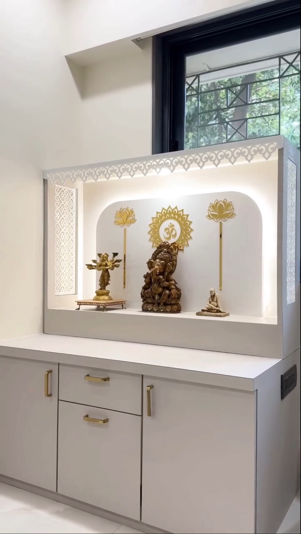 Elegant pooja mandir with Ganesh idol, lotus metal accents, and soft LED cove lighting in a minimalist interior.
