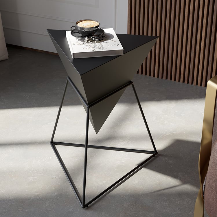 Black metal triangle-base accent table with books and chess set on wooden floor.