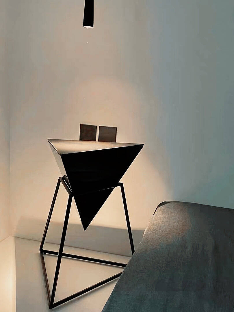 Minimalist pyramid-shaped black side table with glass decor on dark wooden floor.